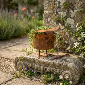 Distressed owl planter with trailing greenery in a garden setting